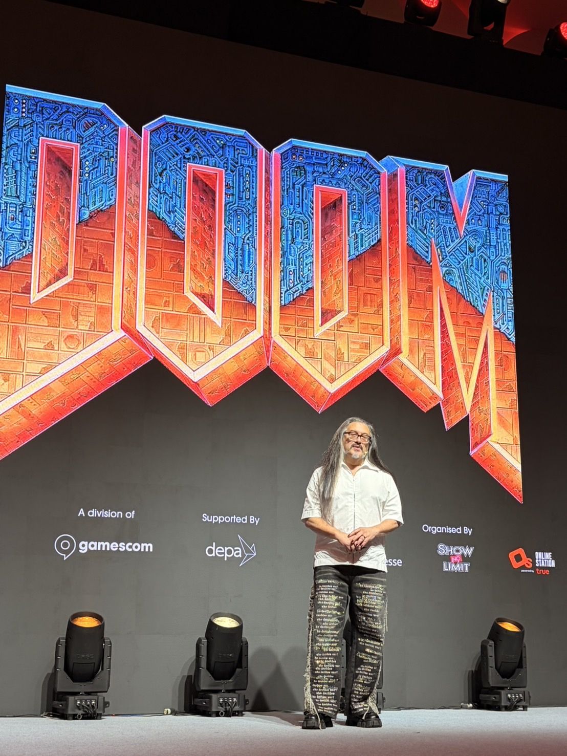 John Romero ขึ้นคีย์โน้ตบนเวทีหน้าโลโก้ Doom ที่งาน gamescom asia x Thailand Game Show 2026